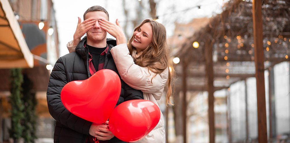 A young, charming girl closes the guy's eyes and smiles. Young couple are having fun. The concept of surprises, valentine's day, gifts, love