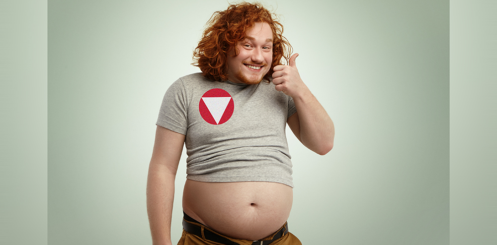 People, nutrition, body shape and healthy lifestyle concept. Happy young plump chubby man with curly ginger hair and beard showing thumps up, saying he is doing okay while his belly sticking out