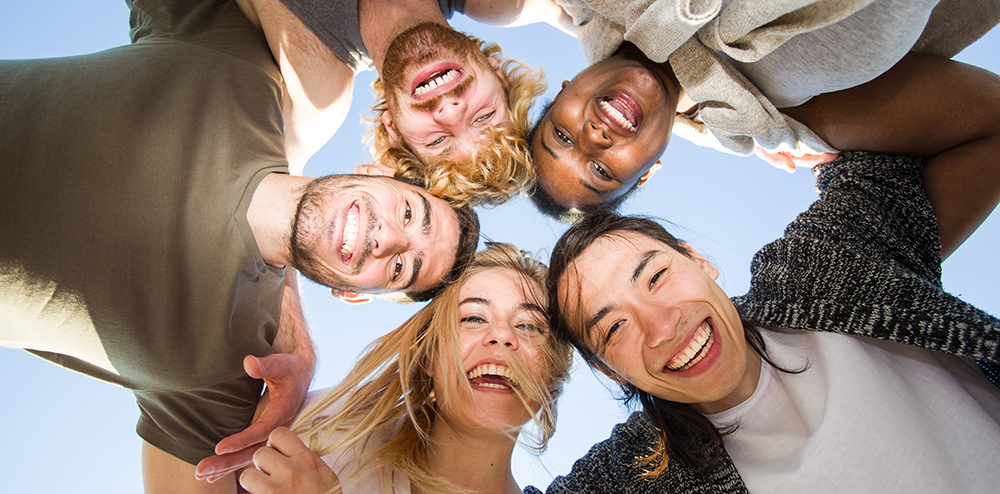 Cheerful friends huddling against blue sky on sunny day