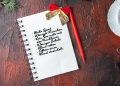 Above view of fir branches a cup of black tea decoration accessories and gift next to notebook with pen on dark background