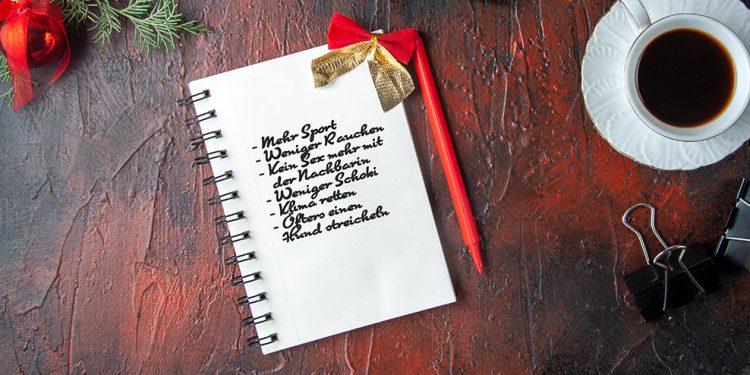 Above view of fir branches a cup of black tea decoration accessories and gift next to notebook with pen on dark background