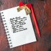 Above view of fir branches a cup of black tea decoration accessories and gift next to notebook with pen on dark background